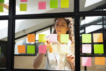 Focused businesswoman writing tasks or ideas on stickers on glass board, confident leader,...