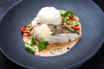 Gebratenes Skrei Kabeljau Fisch Filet in Thai Curry mit Jasmin Reis und Chili als closeup auf einem Modern Design Teller