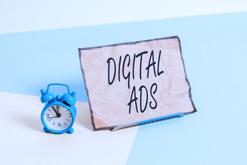 Conceptual hand writing showing Digital Ads. Concept meaning uses the Internet to deliver promotional marketing messages Alarm clock beside a Paper sheet placed on pastel backdrop