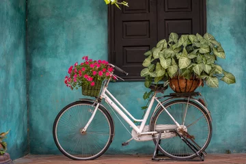 Gordijnen Witte vintage fiets met mand vol bloemen naast een oud gebouw in Danang, Vietnam © OlegD