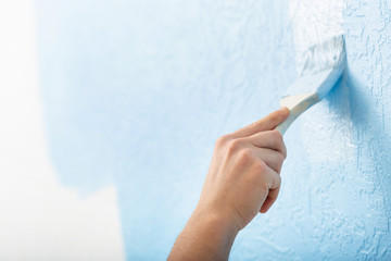 Male hand with brush paints on textured wall