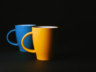 Two ceramic cups on a black isolated background. Yellow and blue ceramic coffee or tea mug. 