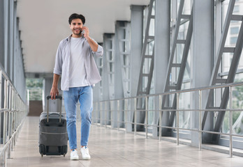 Man traveller walking with luggage in airport and talking on cellphone