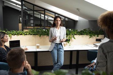 Confident female team leader giving instructions at briefing, mentor training staff, diverse...
