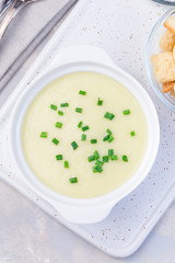 Potato leek soup in white ceramic bowl garnished with green onion served with croutons, vertical, top view, . closeup