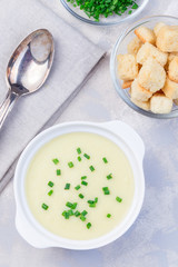 Potato leek soup in white ceramic bowl garnished with green onion served with croutons, vertical,  top view