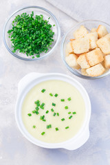 Potato leek soup in white ceramic bowl garnished with green onion served with croutons, vertical, top view