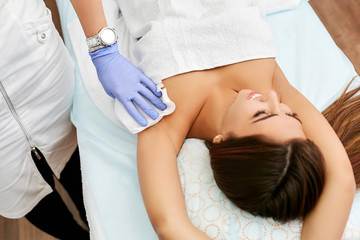 Happy, beautiful brunette in a beauty salon on a sugaring procedure. Girl removes hair from armpits.