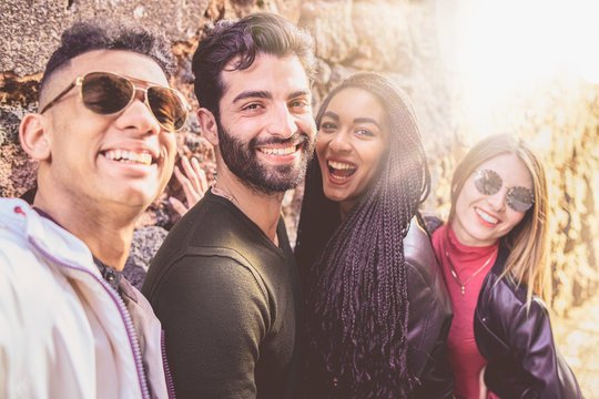 Portrait of a group of young multiracial people having fun taking a selfie with their smartphones. Millennial people outdoors taking self portraits using new technologies in a sunny day.