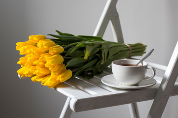bouquet of yellow tulips wrapped in white craft paper lies on a chair