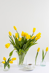 bouquet of yellow tulips is on the table opposite white wall.