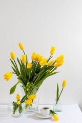 bouquet of yellow tulips is on the table opposite white wall.