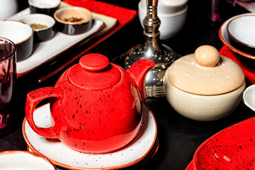 Red porcelain teapot on a black table among other tea utensils.