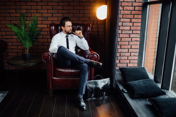 Millionaire man resting and relaxing while sitting on sofa in luxury room. Handsome man smoking...