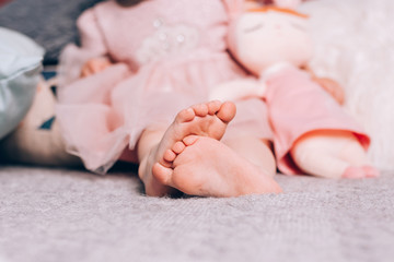 Cute little childs's bare feet lying on warm knitted blanket with soft toy. Cozy time at home, lifestyle.