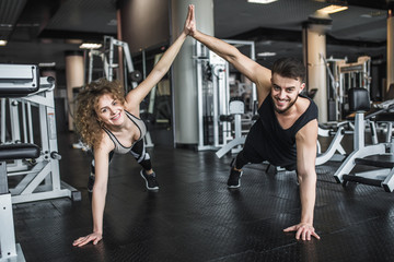 Fototapeta na wymiar Motivated young blond woman and man trainer in middle of workout, standing in plank with give five hands