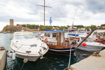 Fototapeta premium Greece. Yachts and boats at the pier on the background of the ancient fortress in Nea fokea. Cassandra. Chalkidiki. Pleasure and fishing boats in the Harbor. An ancient fortress on the coast.