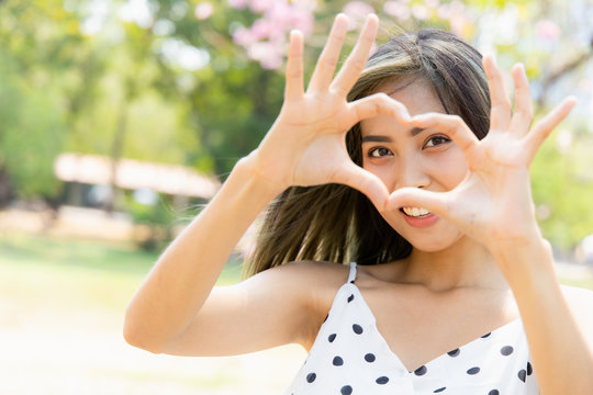 Portrait of a asian young beautiful Holding Heart Shaped Hands Near Eyes Show love. Close Up shots of smiling faces and good skin health.