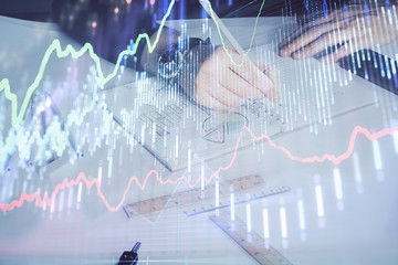 Double exposure of man's hands writing notes of stock market with forex chart.