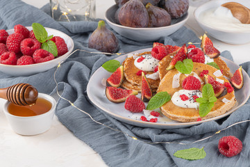 Pancakes with raspberries, figs, yogurt, coconut zest, honey and mint leaves on a plate.