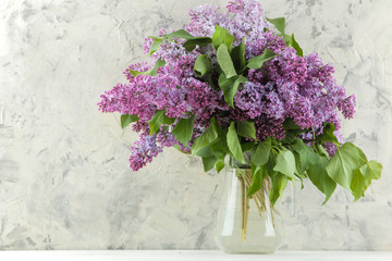 Spring flowers. Twigs of blooming lilac in a vase on a light concrete background