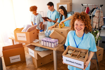 Woman and her colleague working in homeless shelter. Cheerful food drive manager. Happy diverse...