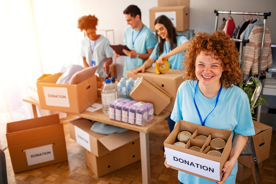 Woman And Her Colleague Working In Homeless Shelter. Cheerful Food Drive Manager. Happy Diverse Group Of Volunteers At Food Bank. Happy Woman Volunteers At A Food Bank