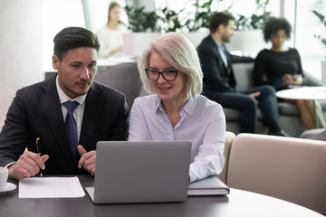 Diverse business partners look at laptop screen discuss company project or startup together, concentrated businesspeople colleagues brainstorm working on computer in office, collaboration concept