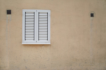 Window closed by white shutters on a beige plastered wall.