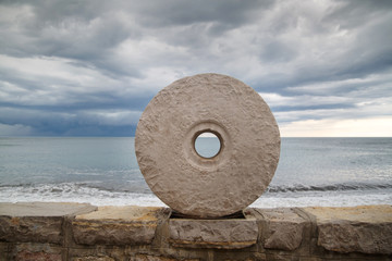 Fototapeta na wymiar Stone millstone on the embankment of the Adriatic Sea against the backdrop of a stormy sea, Montenegro.