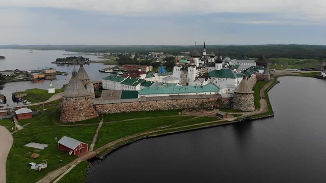 Smooth cinematic flyby of the Solovetsky monastery from the side of the Holy lake with a view of the White sea on a cloudy day with soft lighting. 