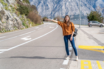 Travel woman hitchhiking. Beautiful young female hitchhiker by the road during vacation trip in mountains Montenegro