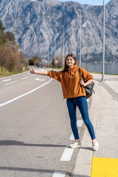 Travel woman hitchhiking. Beautiful young female hitchhiker by the road during vacation trip in mountains Montenegro