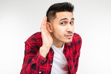 brunette guy in a checkered shirt wide open eavesdrops on a conversation on a white studio...