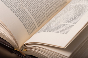 Book pages close up on a light background. Close up side view of a religious Bible book open with gold trim edges resting on a white desk.