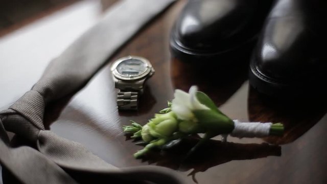 Stylish black leather shoes, silver watch, beige tie and mini bouquet of flowers lie on the table, close-up view. Set of gentleman for important meeting. Groom getting ready in morning before wedding.