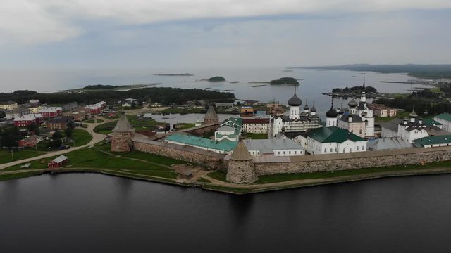 Smooth cinematic flyby of the Solovetsky monastery from the side of the Holy lake with a view of the White sea on a cloudy day with soft lighting. 