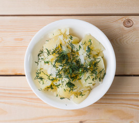 Boiled potatoes with dill in a white bowl on the boards. View from above
