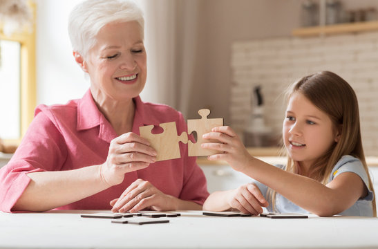 Lovely girl and her grandma solving jigsaw puzzle together at home - Powered by Adobe