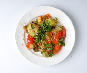 Hot salad of zucchini and pepper on a round white plate. Top view