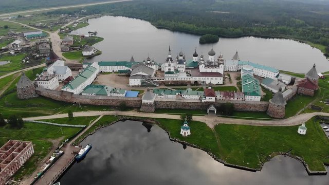 Smooth cinematic flyby of the Solovetsky monastery from the side of the White sea with a view of the Saint Lake on a cloudy day with soft lighting. 