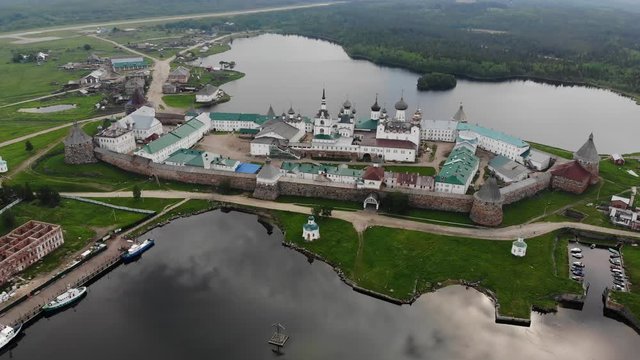 Smooth cinematic flyby of the Solovetsky monastery from the side of the White sea with a view of the Saint Lake on a cloudy day with soft lighting. 