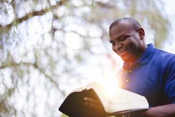 African-American male reading the Bible and smiling at the park on a sunny day