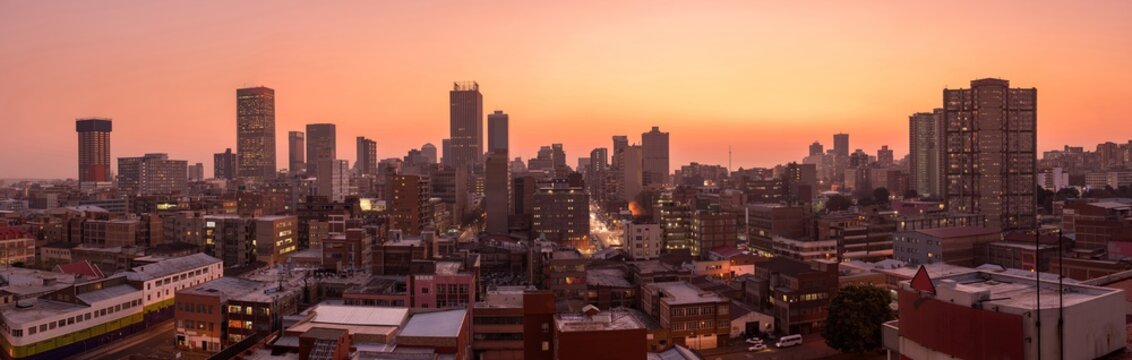 A beautiful and dramatic panoramic photograph of the Johannesburg city skyline, taken on a golden evening after sunset.