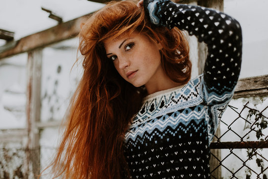 Winter fashion. Beauty girl portrait red hair young woman in warm clothing outdoor enjoying sunlight on sunny day. City Gdansk in the background