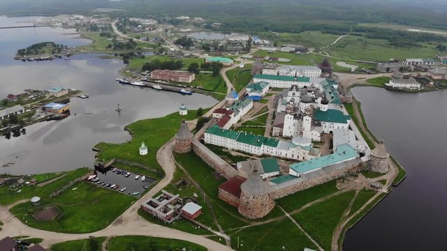 Smooth cinematic flyby of the Solovetsky monastery from the south side with a view of the White sea, Saint Lake and nearby village on a cloudy day with soft lighting. 