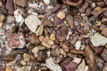Multicolor stones of different shapes and size. Small rocks on beach sand close up.