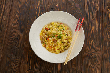 Delicious asian fried rice with beef, egg, carrot, garlic and green onion with chopsticks horizontal view from above on wooden table white plate, copy space