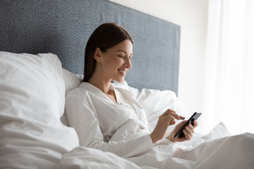 Side view happy attractive brunette woman using mobile phone after wake up, enjoying good morning...