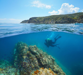 Mediterranean sea scuba diving, two divers underwater and rocky coastline in the Marine reserve of...